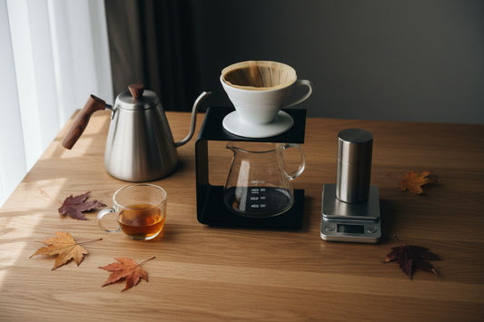 Pour over coffee setup with scale, dripper stand, and gooseneck kettle on a wood surface with autumn leaves
