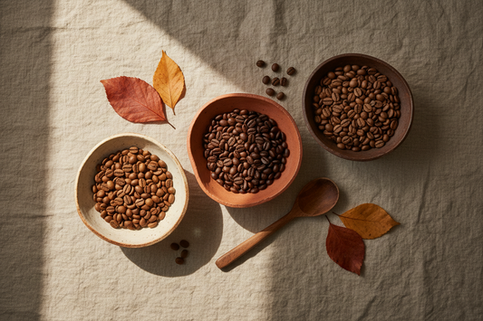 Assorted single origin coffee beans from Ethiopia, Colombia, and Guatemala displayed in ceramic bowls on a linen surface with autumn leaves