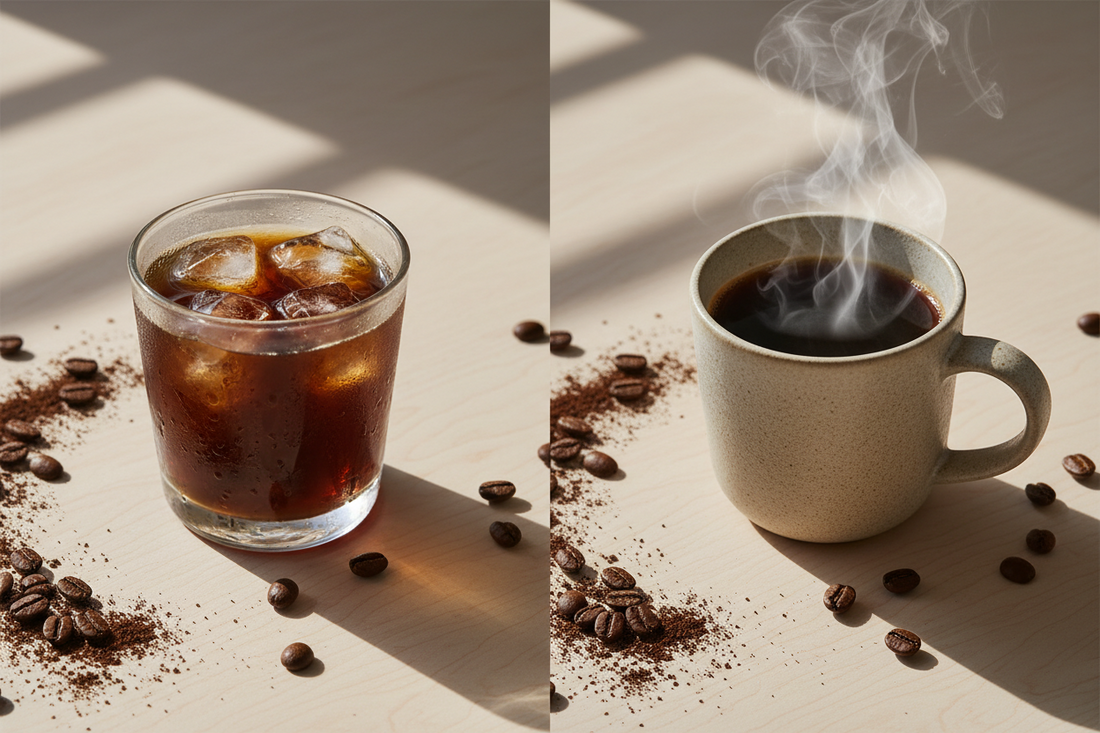 Cold brew coffee over ice next to a steaming hot ceramic mug on a wood surface, comparing two coffee brewing styles